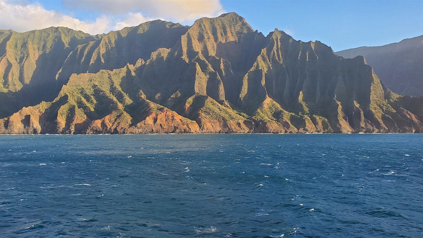Open ocean beside the steep green cliffs of the Kauai coast