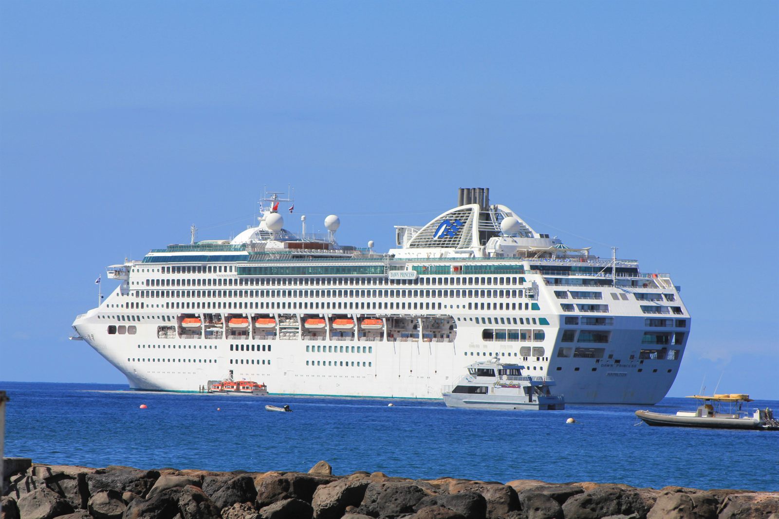 Large white cruise ship at sea off a rocky shoreline